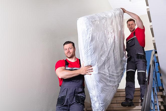 two workers safely transporting a box spring out of a house in Cambridge